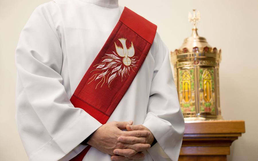 A deacon in alb and red diaconal stole standing near the tabernacle