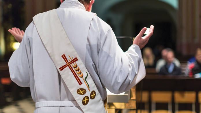 A deacon in a white stole facing the congregation at the ambo