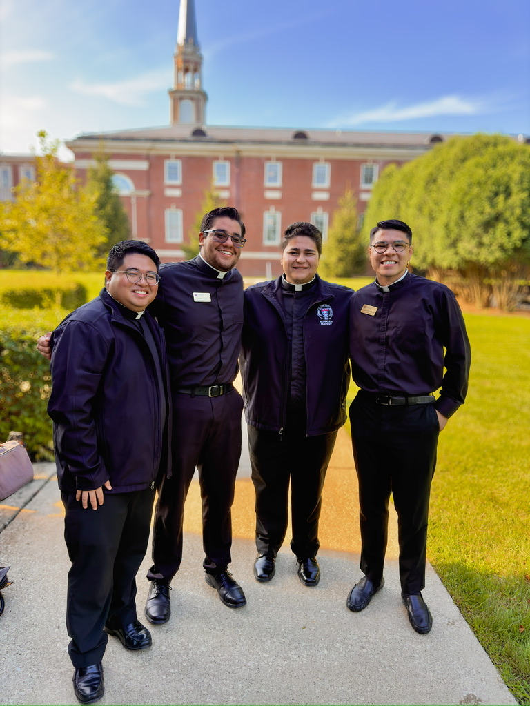 Four men in clerical attire standing together outside a seminary